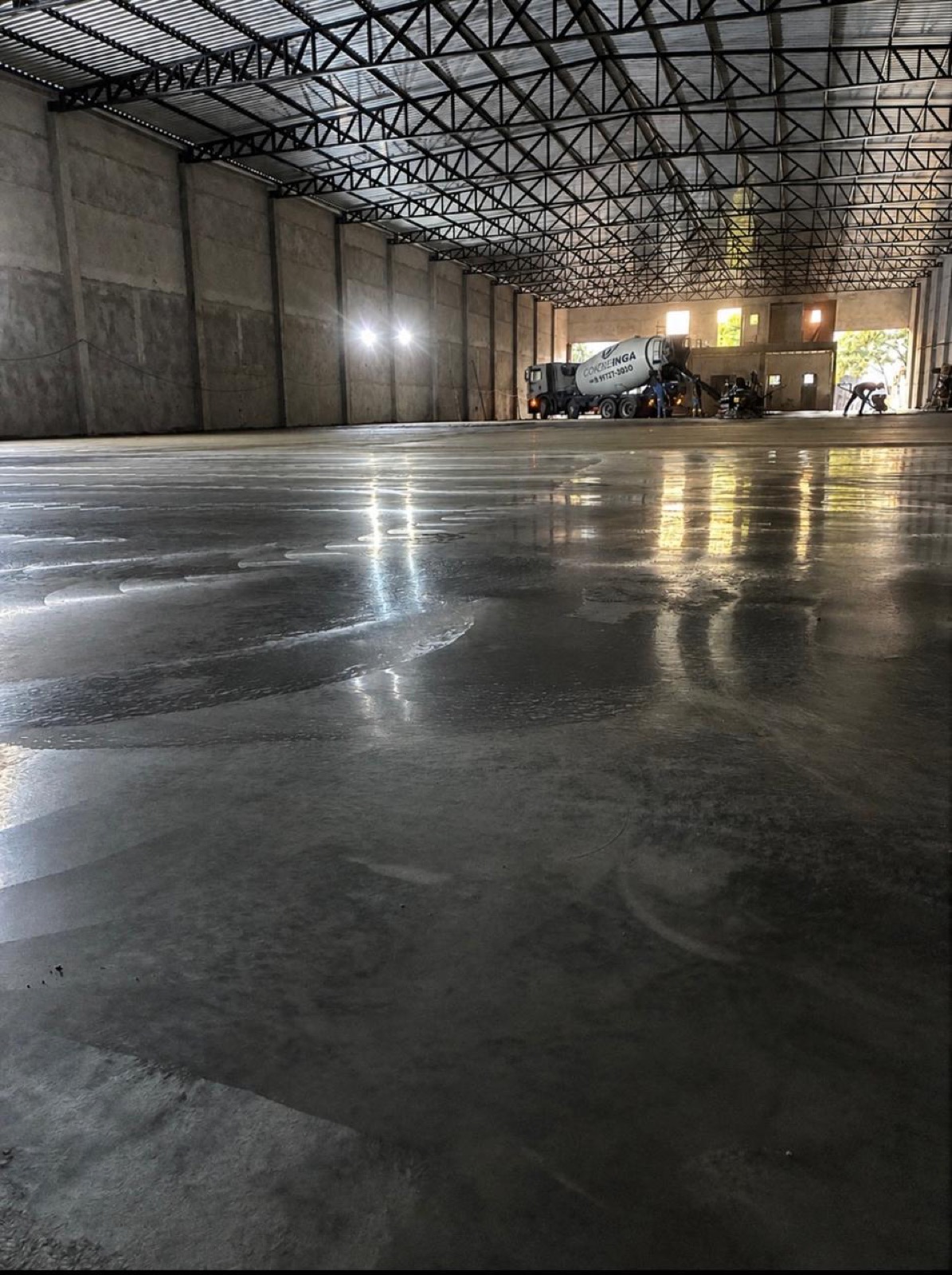 galpão industrial com piso de concreto polido executado pela Brito e Pauluci em Maringá, com caminhão betoneira e equipe ao fundo